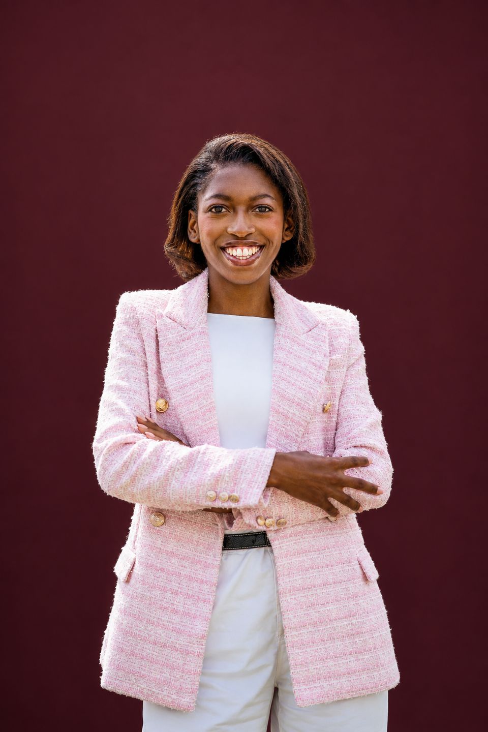 Naledi Ncube in a pink tweed blazer, arms folded, smiling against a burgundy backdrop